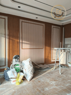 Phòng khách đang thi công, trần giật cấp bo cong trắng, vách nano lam gỗ hai bên, cửa sổ lớn nhìn ra ngoài